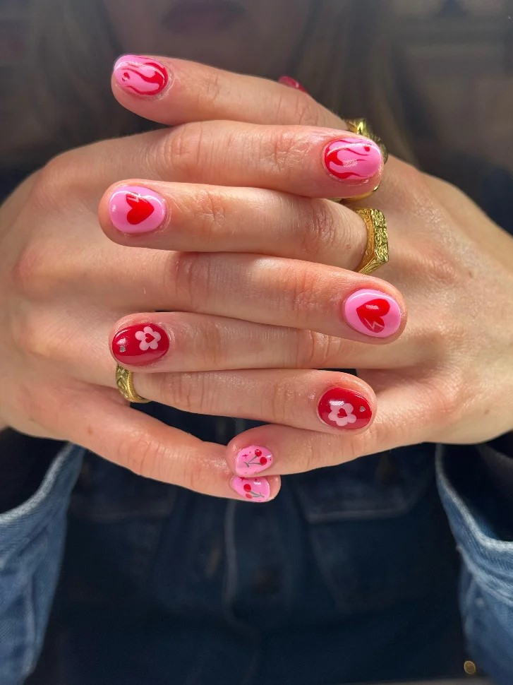 A womans hands clasped together a bright pink and red BIAB manicure with nail art