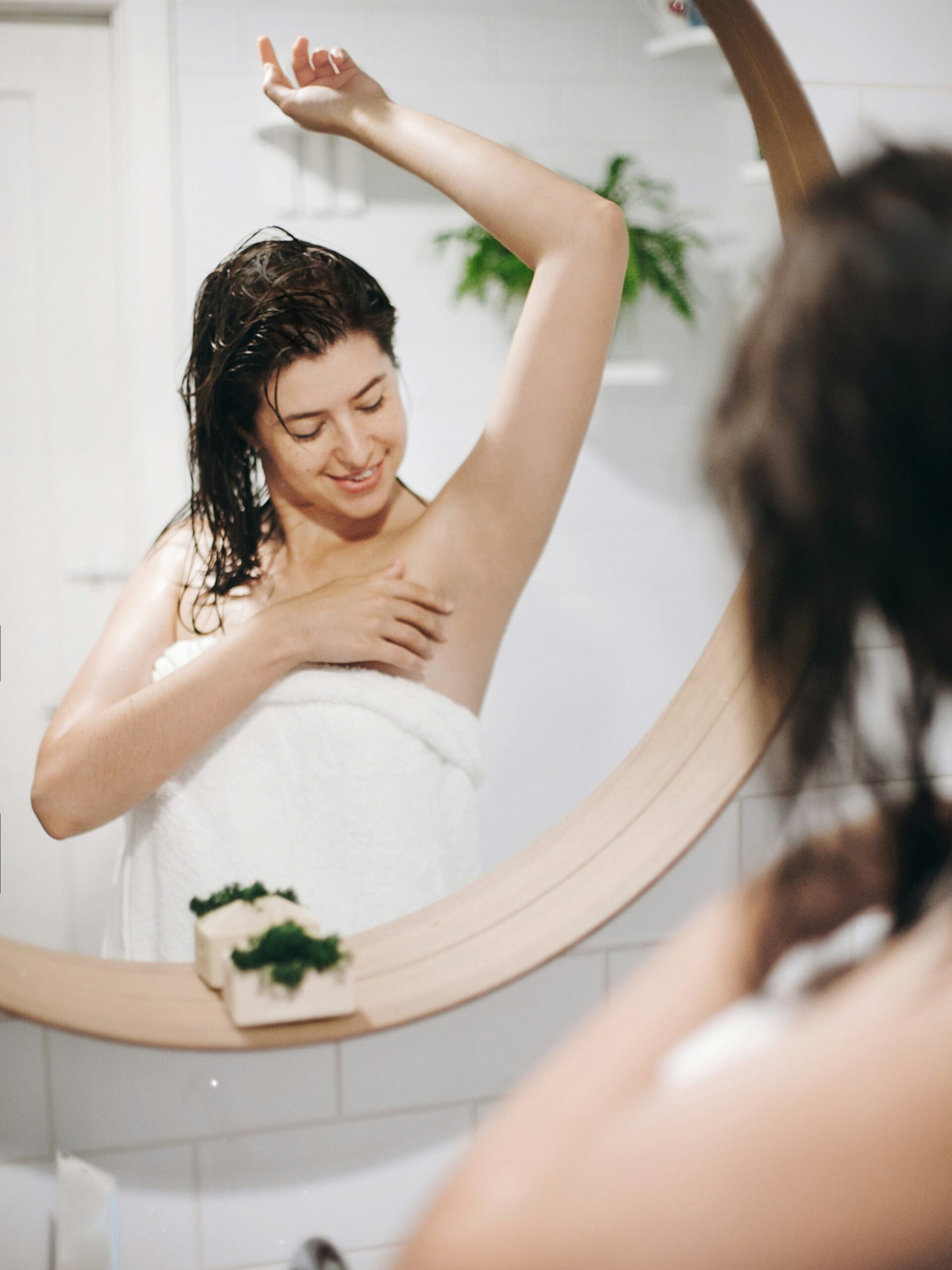 Woman wearing a bath towel and admiring her smooth armpits in the mirror after IPL treatment