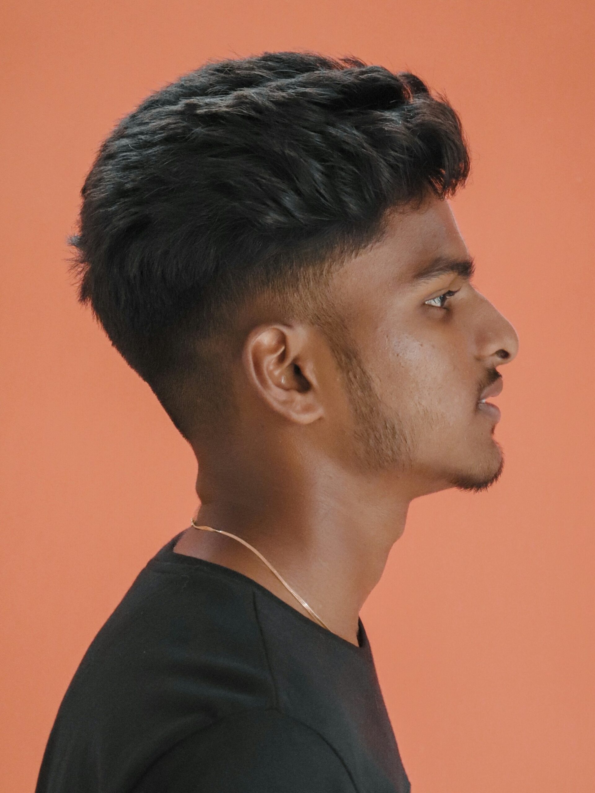 Side profile portrait of a man with a textured volume hairstyle paired with a low taper fade