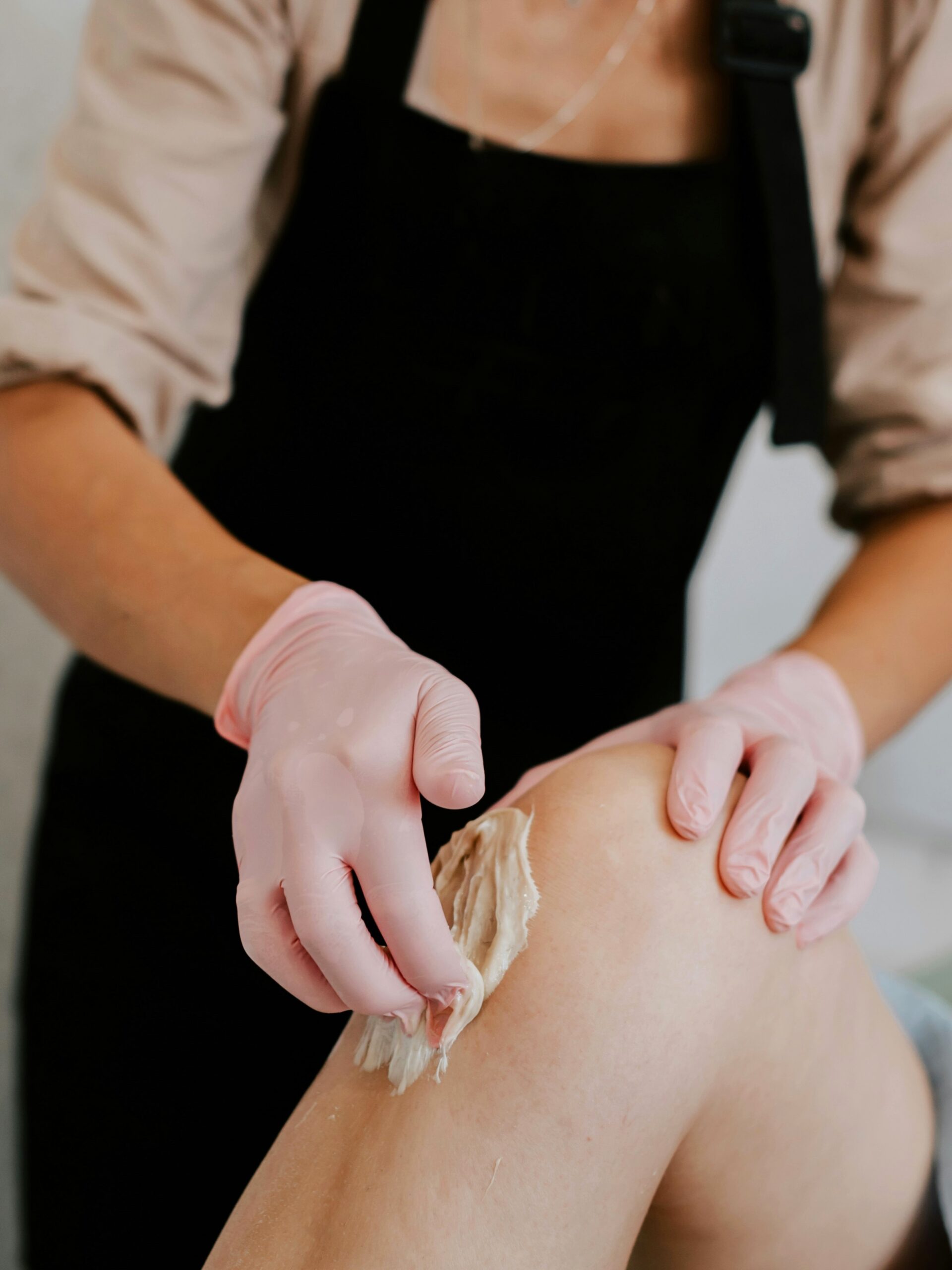 Side view of practitioner applying wax to a client's leg as she lies comfortably on a treatment bed in salon