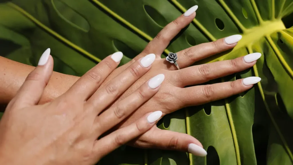 tudio shot of fresh almond-shaped nude-colour acrylic nails on a palm leaf backdrop