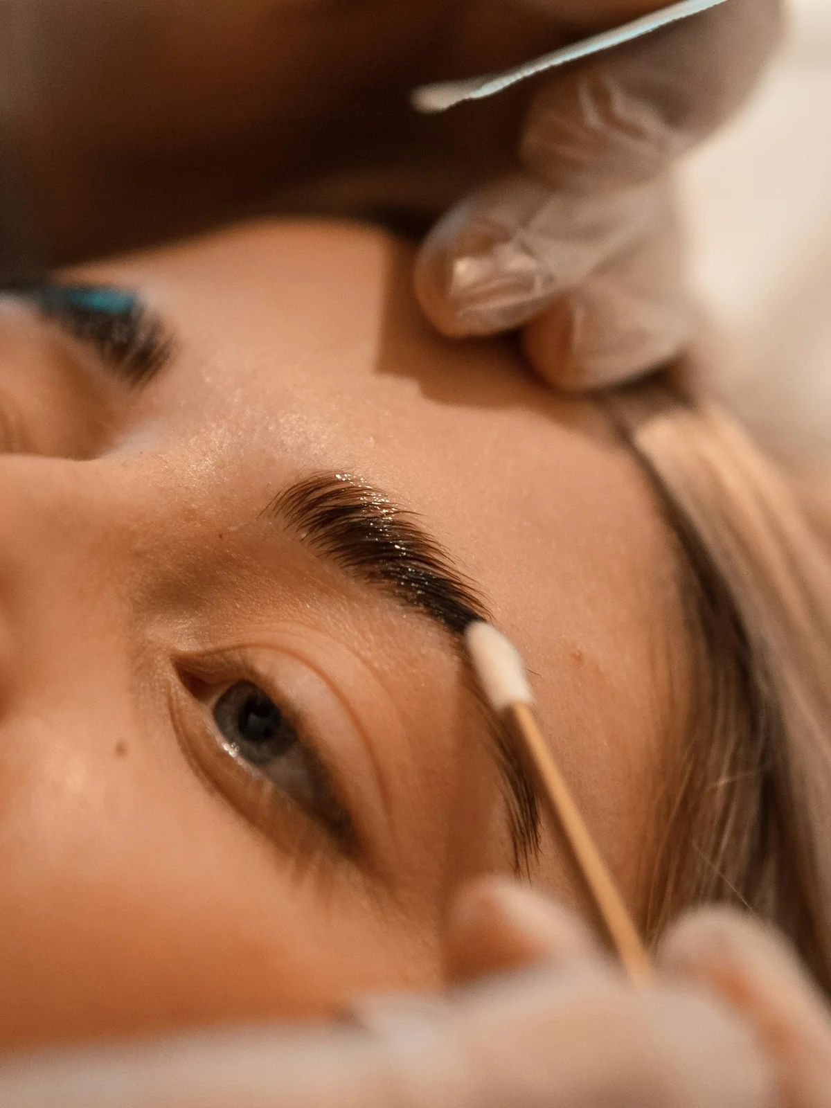Close-up of a client lying down as a technician applies brow lamination treatment