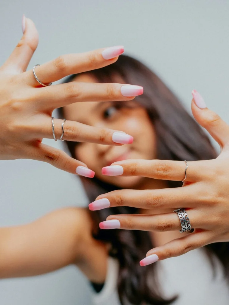 A woman holds her hands to the camera showing an ombre French tips manicure with a pale pink base and shocking pink tips on coffin-shaped nails