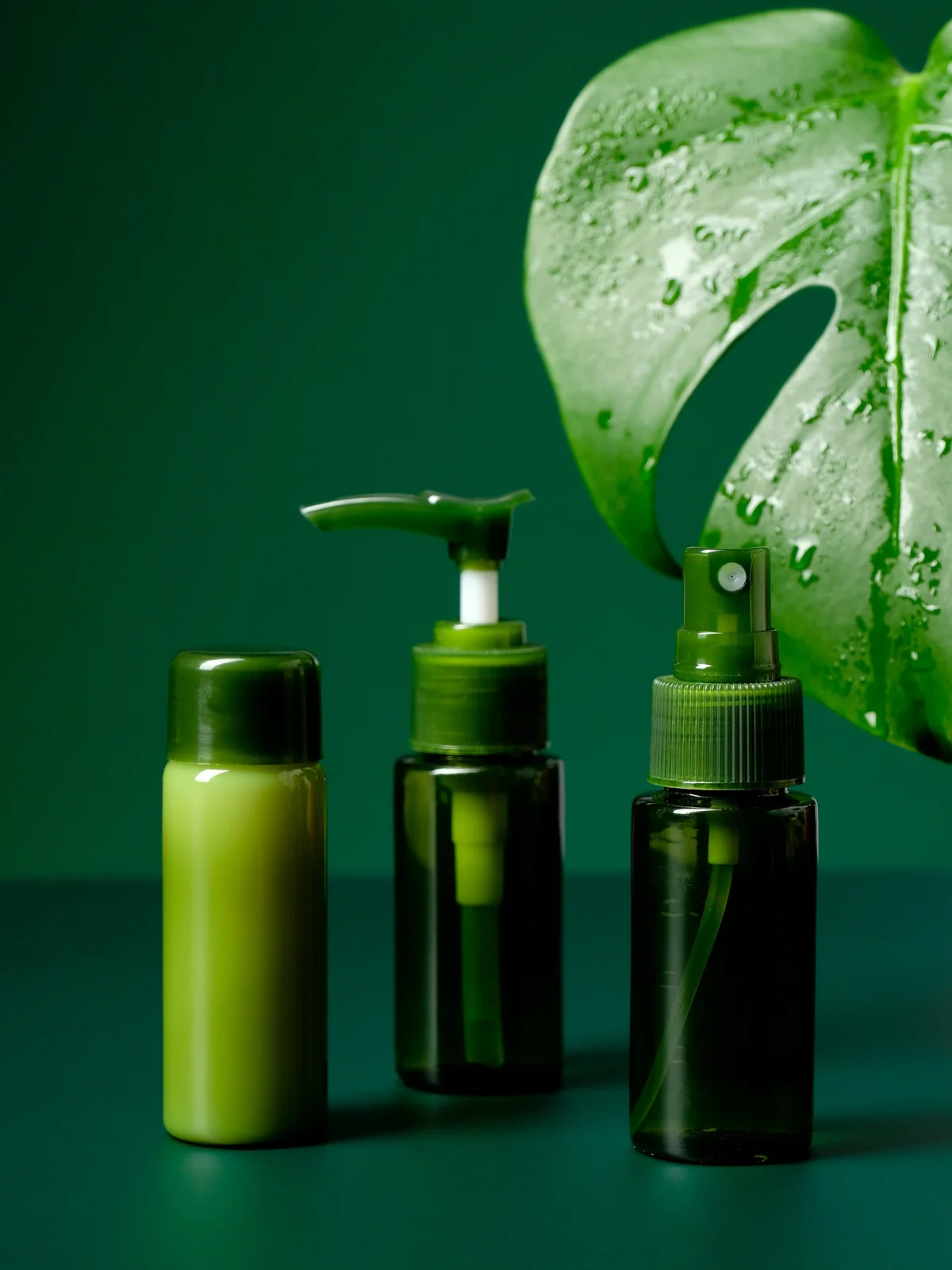 Product shot of three soothing gels and creams in green bottles with a large tropical green leaf in the background