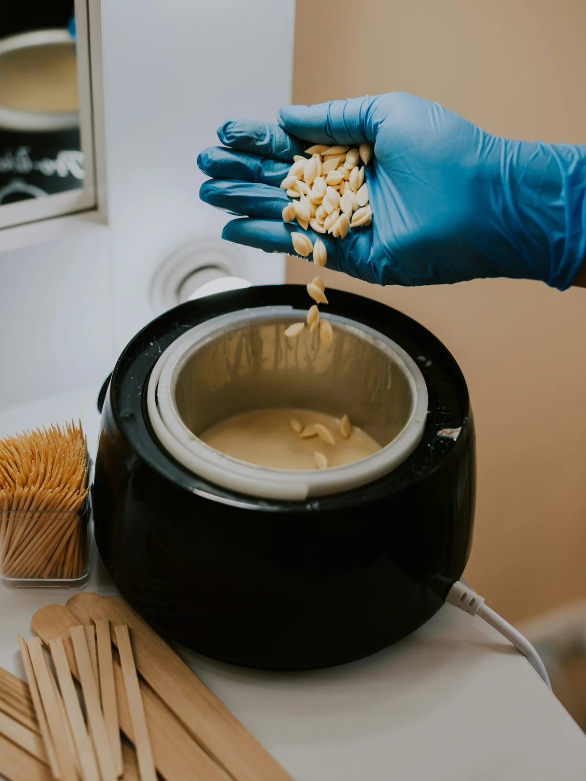 Close-up of a therapist’s gloved hand stirring hot wax beads into a pot of hot wax ready for a client appointment
