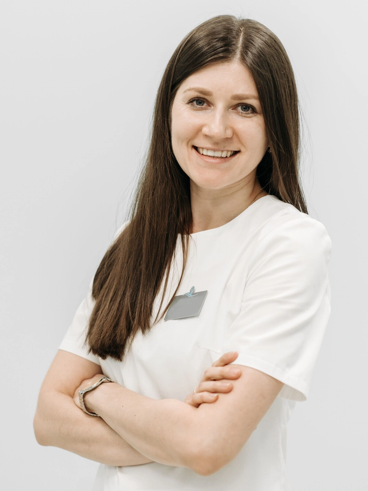 Portrait of an aesthetician wearing a white tunic and smiling with her arms folded